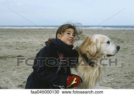 Stock Image - Young girl with dog on beach flying kite. Fotosearch