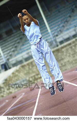 Stock Photo - Young woman doing jumping exercises on track. Fotosearch
