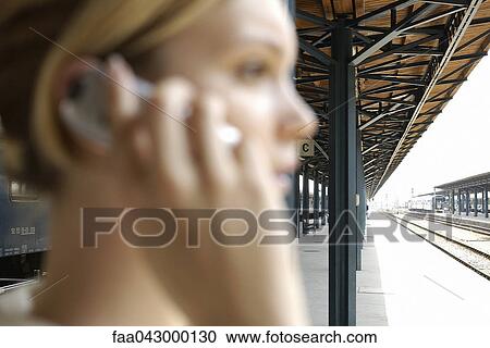 Stock Image - Young woman on train platform phoning. Fotosearch