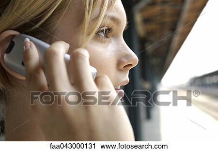 Stock Image - Young woman on train platform phoning. Fotosearch