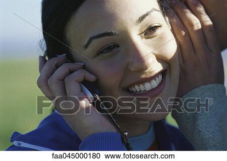 Young woman using cell phone, man whispering in her ear View Large Photo Image Stock Image - Young woman using cell phone, man whispering in her ear. Fotosearch