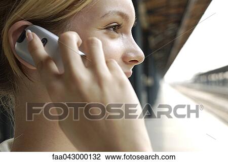 Stock Image - Young woman with pleased facial expression on train platform phoning. Fotosearch