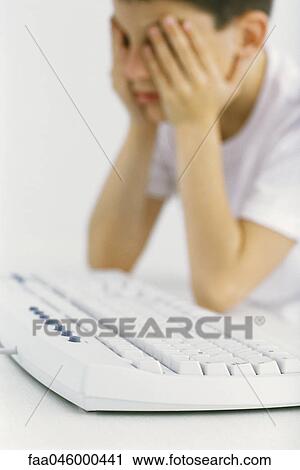 Boy at computer keyboard holding head View Large Photo Image Stock Image - Boy at computer keyboard holding head. Fotosearch
