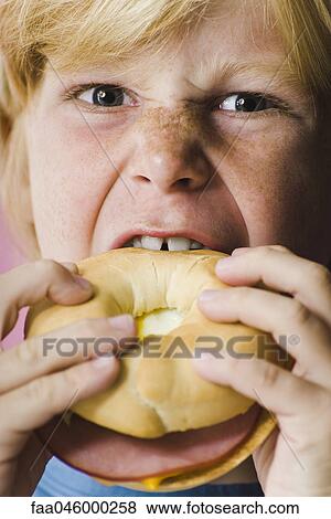 Stock Photo - Boy biting into ham and cheese bagel sandwich, close-up. Fotosearch