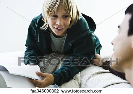 Stock Image - Boy leaning against sofa talking to older brother. Fotosearch