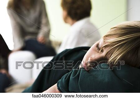Stock Photo - Boy resting head on arms sleeping, family members in background. Fotosearch