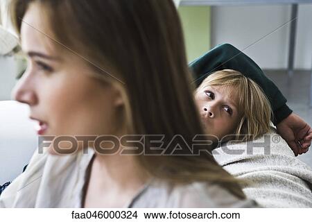 Boy sitting on sofa, looking over shoulder, woman in foreground View Large Photo Image Picture - Boy sitting on sofa, looking over shoulder, woman in foreground. Fotosearch