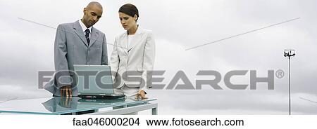 Business associates standing together outdoors, looking at laptop computer View Large Photo Image Picture - Business associates standing together outdoors, looking at laptop computer. Fotosearch