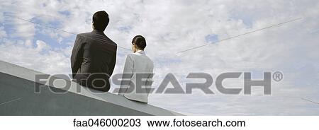 Businessman and businesswoman sitting side by side on rooftop ledge View Large Photo Image Stock Image - Businessman and businesswoman sitting side by side on rooftop ledge. Fotosearch