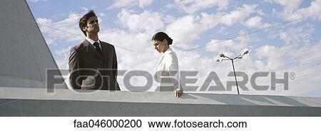 Businessman and businesswoman standing on rooftop, man looking at view, woman looking down View Large Photo Image Stock Image - Businessman and businesswoman standing on rooftop, man looking at view, woman looking down. Fotosearch