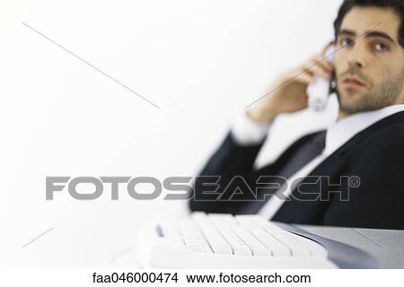 Picture - Businessman on phone call, looking away, keyboard in foreground. Fotosearch