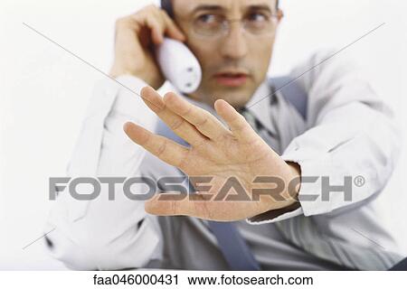 Stock Image - Businessman on phone call making stop gesture with hand. Fotosearch