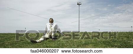 Stock Photo - Businessman sitting in grass, leaning back enjoying sunny spell. Fotosearch