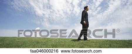 Businessman walking barefoot in grassy field, empty chair nearby View Large Photo Image Stock Photograph - Businessman walking barefoot in grassy field, empty chair nearby. Fotosearch