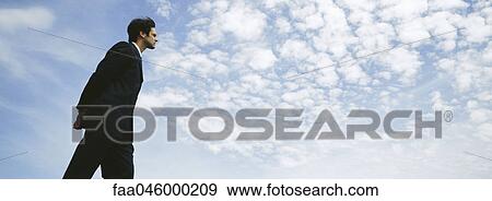 Businessman walking outdoors with hands behind back, low angle view View Large Photo Image Stock Photo - Businessman walking outdoors with hands behind back, low angle view. Fotosearch