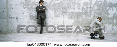 Businessman with arms folded leaning against wall watching associate ride child's tricycle View Large Photo Image Picture - Businessman with arms folded leaning against wall watching associate ride child's tricycle. Fotosearch