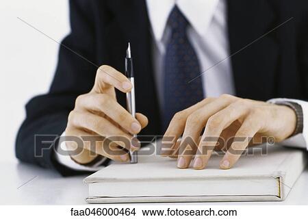 Picture - Businessman's hands on book, holding pen, cropped view. Fotosearch