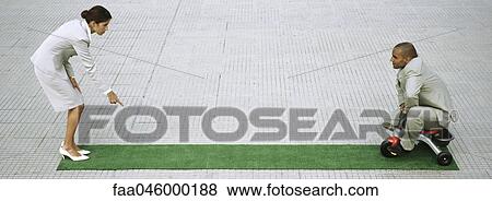 Stock Photo - Businesswoman leaning forward pointing sternly at ground, man pedaling tricycle towards her. Fotosearch