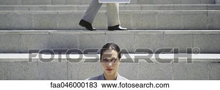 Businesswoman on steps, looking at camera, man walking in background View Large Photo Image Stock Image - Businesswoman on steps, looking at camera, man walking in background. Fotosearch