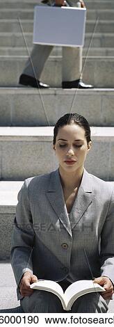 Stock Image - Businesswoman sitting outdoors holding book, eyes closed. Fotosearch