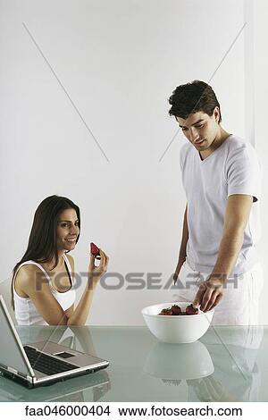 Picture - Couple eating strawberries, laptop nearby. Fotosearch