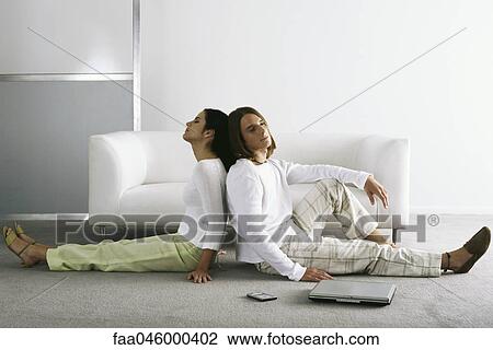 Stock Image - Couple sitting back to back on floor. Fotosearch