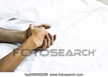 Couple's clasped hands on bed View Large Photo Image Stock Photo - Couple's clasped hands on bed. Fotosearch