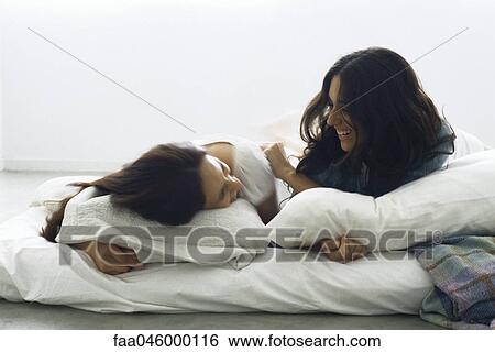 Stock Photograph - Female friends lying in bed together laughing. Fotosearch