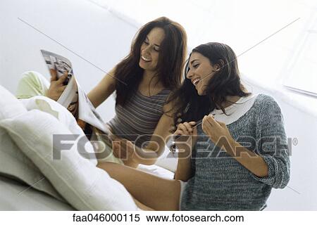 Female friends sitting in bed together, looking at magazine View Large Photo Image Stock Photography - Female friends sitting in bed together, looking at magazine. Fotosearch