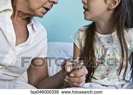 Stock Photo - Grandmother and young granddaughter holding hands and talking, cropped. Fotosearch