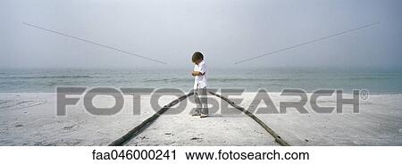 Stock Image - Little boy sulking on beach, arms folded. Fotosearch