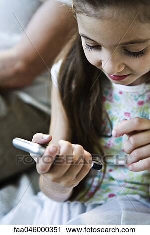 Stock Image - Little girl looking at cell phone, woman in background. Fotosearch