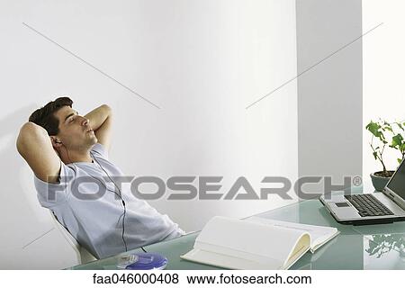 Man at desk leaning back with hands behind head, listening to earphones and whistling View Large Photo Image Stock Photo - Man at desk leaning back with hands behind head, listening to earphones and whistling. Fotosearch