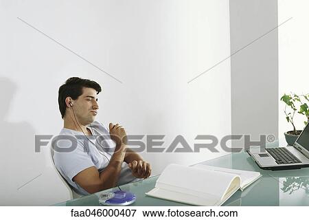 Stock Photo - Man at desk listening to music, pretending to play drums along with song. Fotosearch