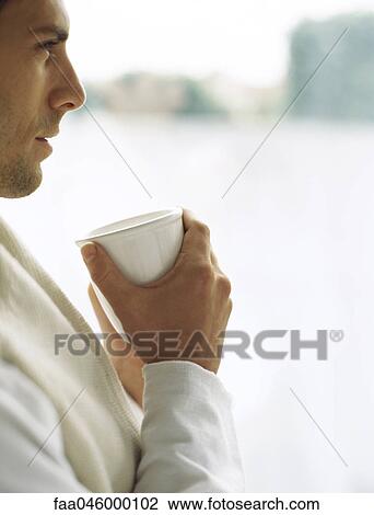 Stock Image - Man holding cup of coffee, looking away in thought. Fotosearch