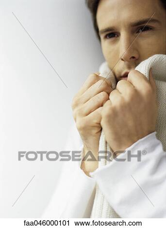 Stock Image - Man holding ends of scarf close to face. Fotosearch