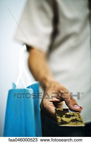 Stock Image - Man paying for purchase with credit card, cropped, close-up. Fotosearch