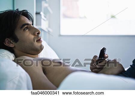 Man reclining on bed holding cell phone, looking away contemplatively View Large Photo Image Stock Image - Man reclining on bed holding cell phone, looking away contemplatively. Fotosearch