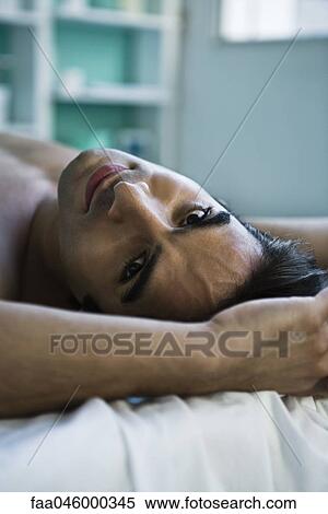 Man reclining on bed, looking at camera View Large Photo Image Stock Photography - Man reclining on bed, looking at camera. Fotosearch