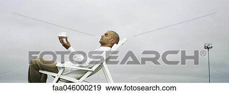 Man relaxing in deckchair, holding up coffee cup View Large Photo Image Stock Photo - Man relaxing in deckchair, holding up coffee cup. Fotosearch