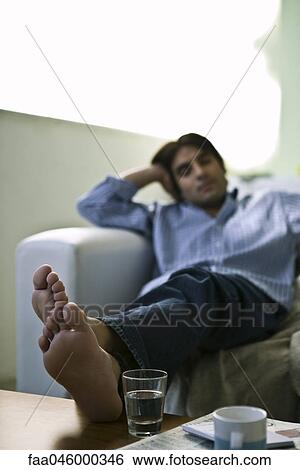 Man sitting on sofa with feet up on coffee table View Large Photo Image Stock Photograph - Man sitting on sofa with feet up on coffee table. Fotosearch