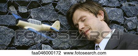 Stock Image - Man with eyes closed, smiling, leaning head against wall, toy airplane in foreground. Fotosearch