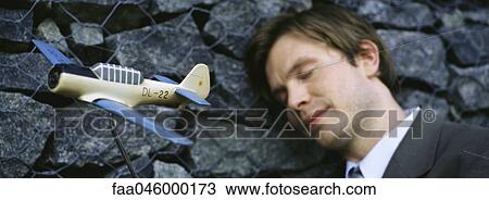 Stock Image - Man with eyes closed, smiling, leaning head against wall, toy airplane in foreground. Fotosearch