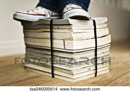 Picture - Person standing on top of bound stack of paper catalogs and magazines. Fotosearch