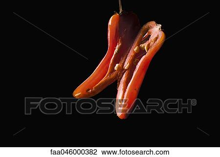 Stock Image - Red chili pepper sliced in half lengthwise, on black background. Fotosearch