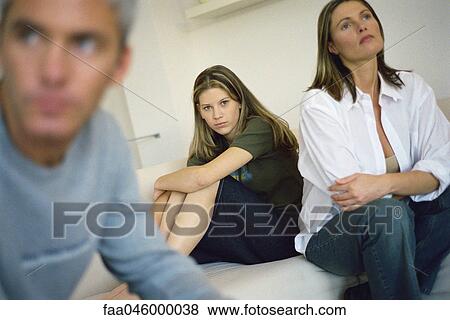 Teenage girl sitting on bed hugging knees, parents sitting nearby looking away with air of frustration View Large Photo Image Stock Photo - Teenage girl sitting on bed hugging knees, parents sitting nearby looking away with air of frustration. Fotosearch