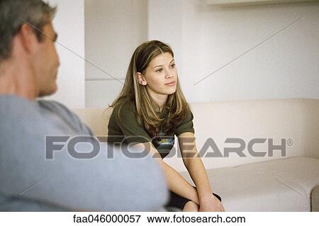 Teenage girl sitting on sofa contemplatively looking away, father in foreground View Large Photo Image Stock Photo - Teenage girl sitting on sofa contemplatively looking away, father in foreground. Fotosearch