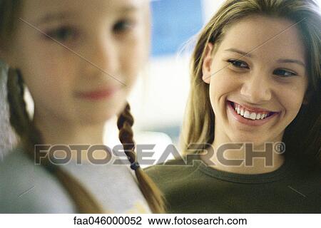Stock Image - Teenage girl smiling at younger sister in foreground. Fotosearch
