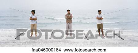 Three men with arms defiantly folded standing on beach, separated one from the other by lengths of wood View Large Photo Image Picture - Three men with arms defiantly folded standing on beach, separated one from the other by lengths of wood. Fotosearch