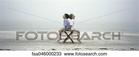 Two boys sitting back to back on chair on beach View Large Photo Image Stock Image - Two boys sitting back to back on chair on beach. Fotosearch